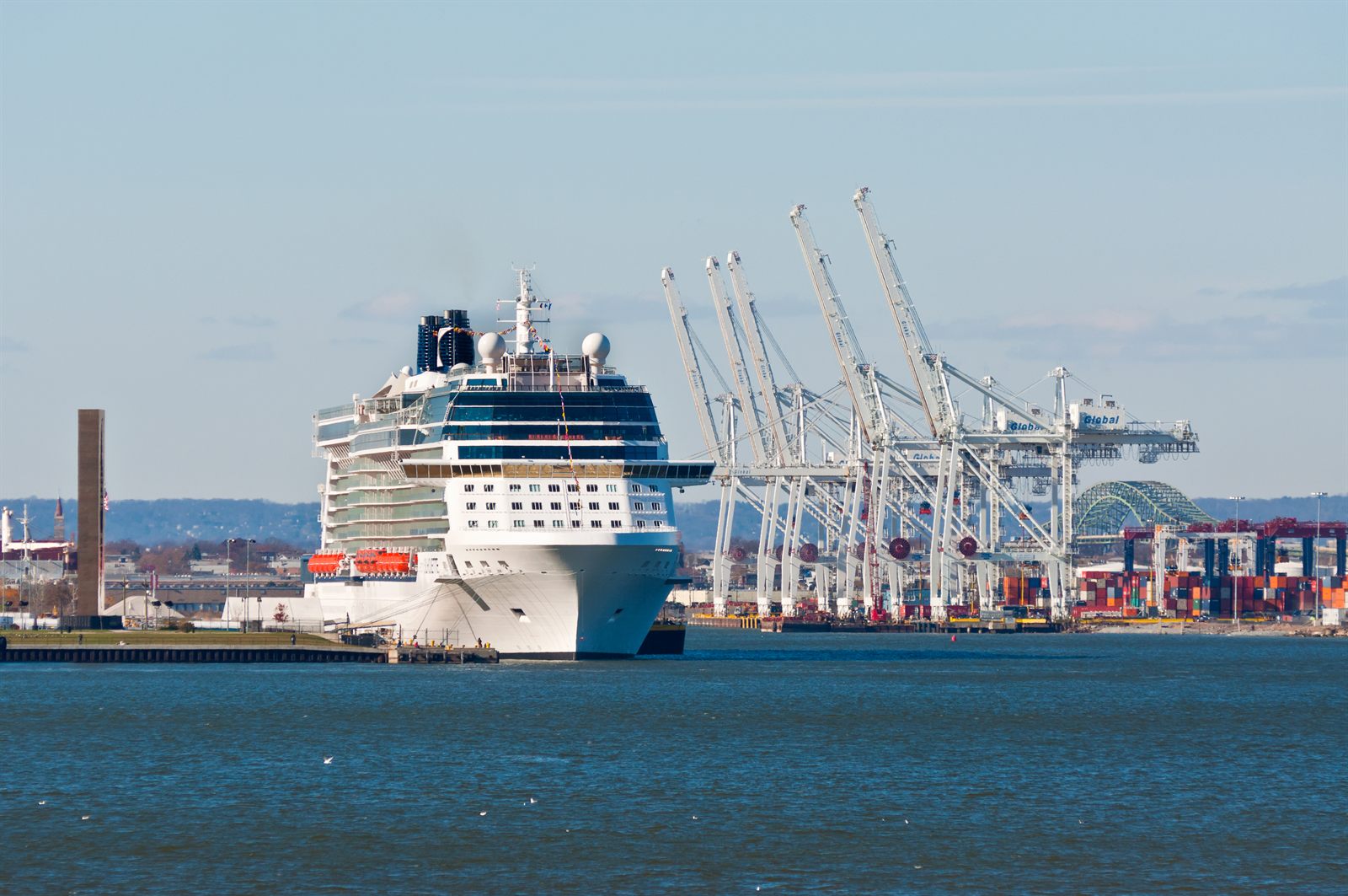 Cruise ship berthed at a busy port with cranes behind it