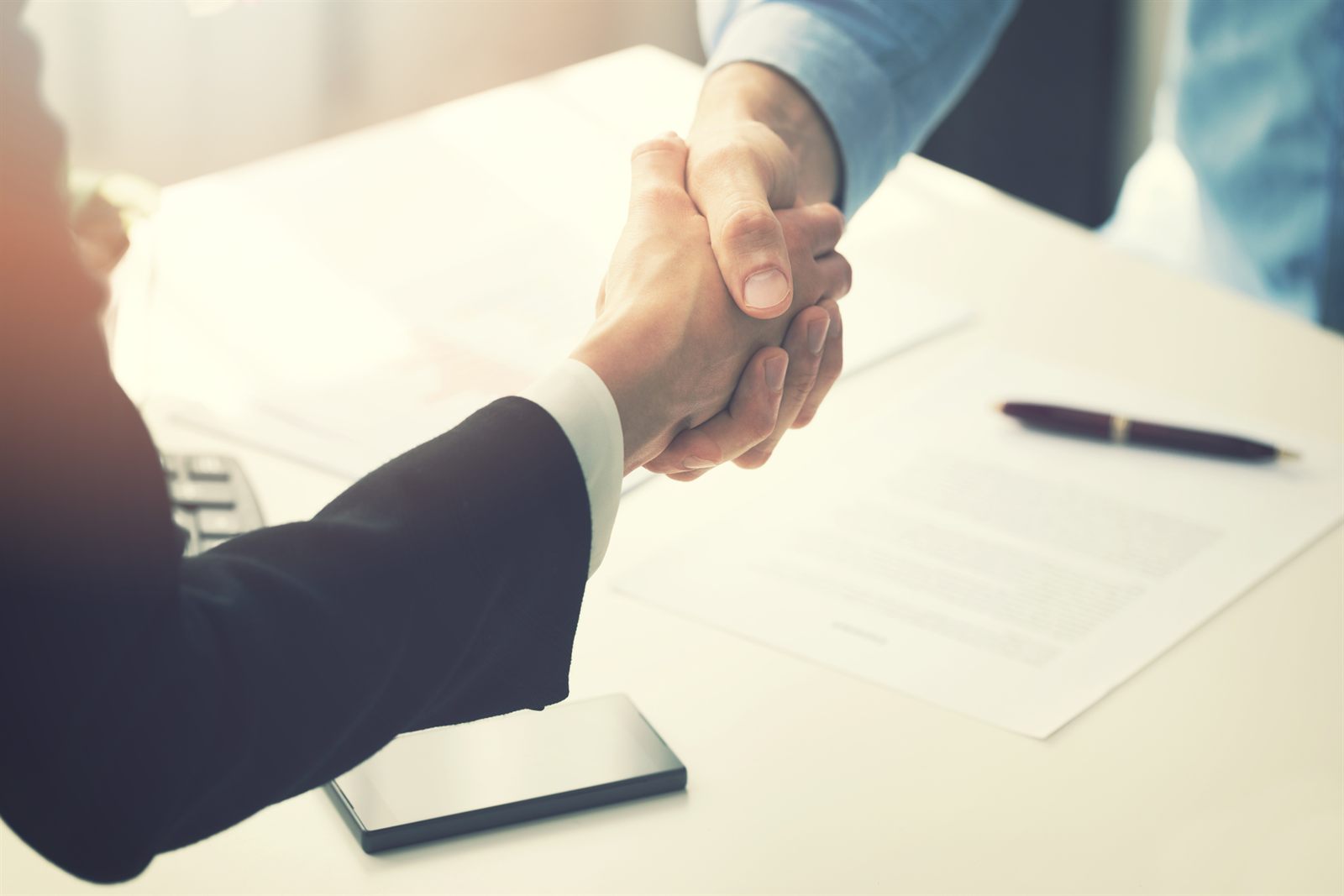 Handshake over a signed agreement on a desk